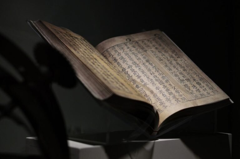 An-old-book-with-vertical-columns-of-Chinese-characters-is-displayed-open-on-a-stand-under-dim-lighting