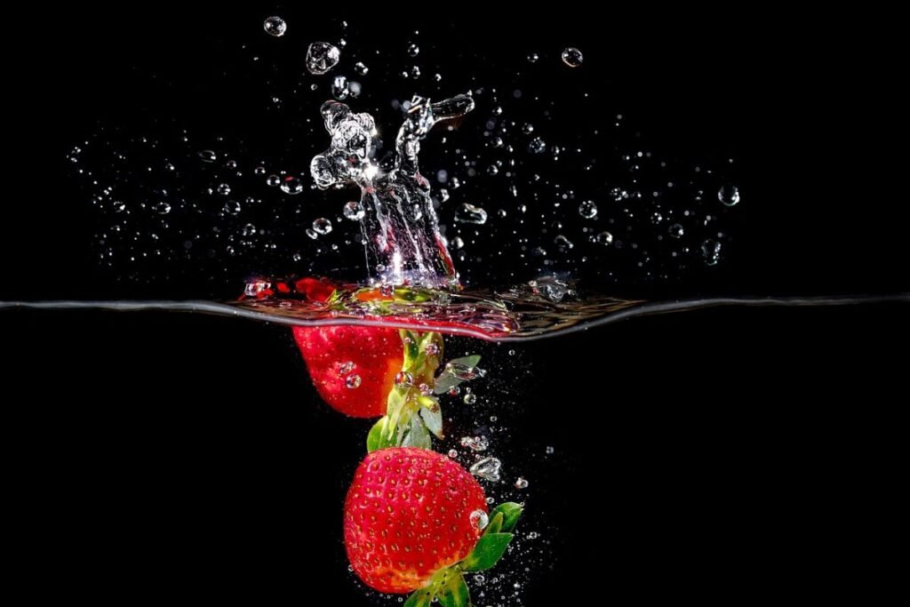 Two strawberries submerged in water, creating splashes and bubbles against a black background.