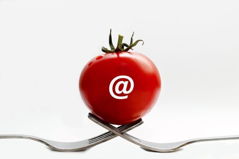 Red tomato with an '@' symbol placed on two crossed forks, creating a unique visual composition.